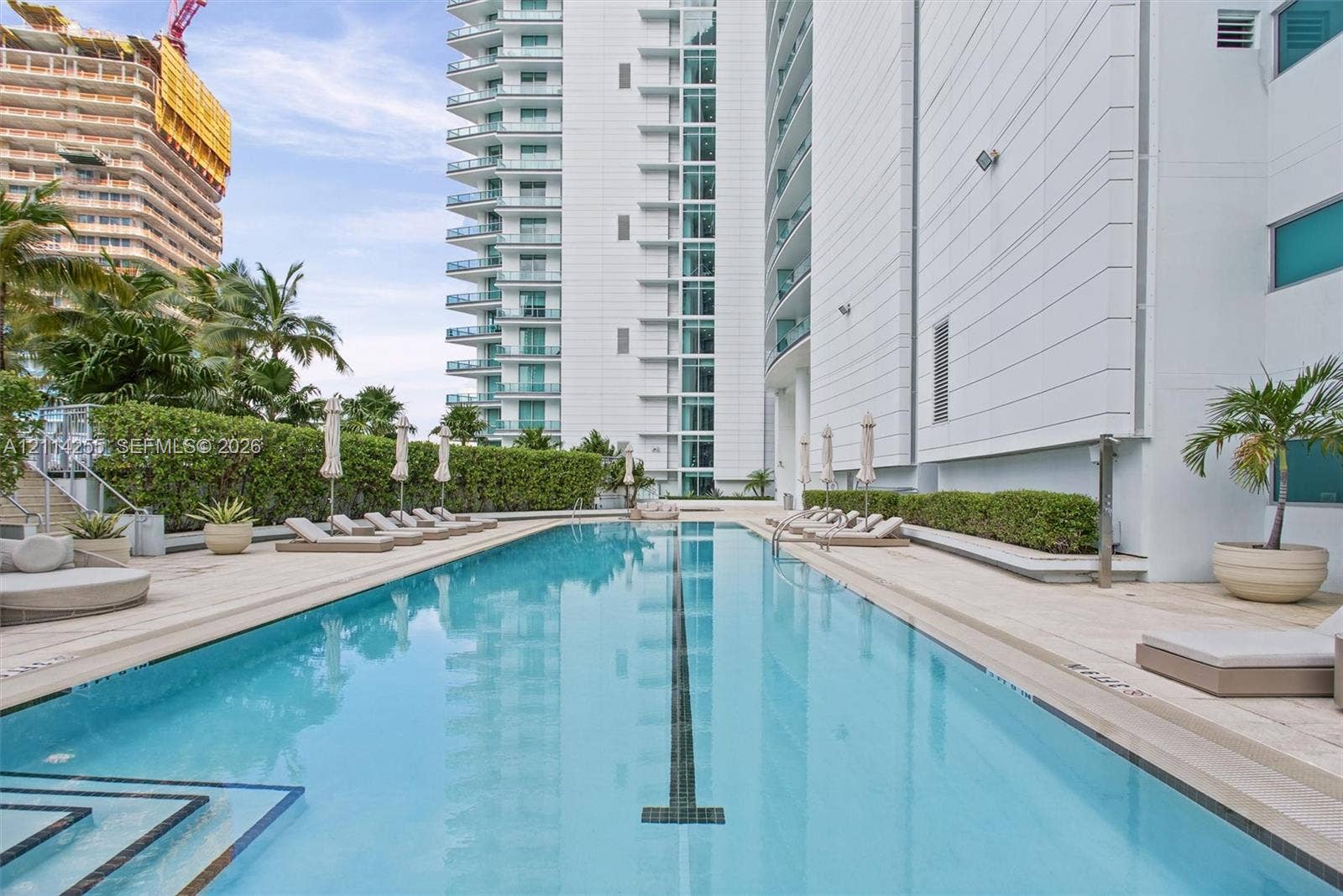 900 Biscayne Boulevard, #1705, Miami, FL 33132 Lap pool featuring a stone-paver deck, built-in tile lane marker, manicured hedges, and high-rise building exterior