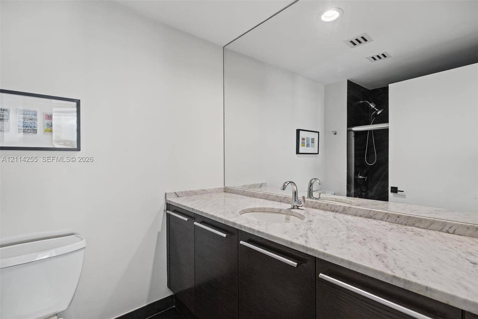 900 Biscayne Boulevard, #1705, Miami, FL 33132 Bathroom featuring dark wood-finish cabinetry, stone countertop with an integrated oval sink, chrome faucet, expansive wall-to-wall mirror, and recessed lighting
