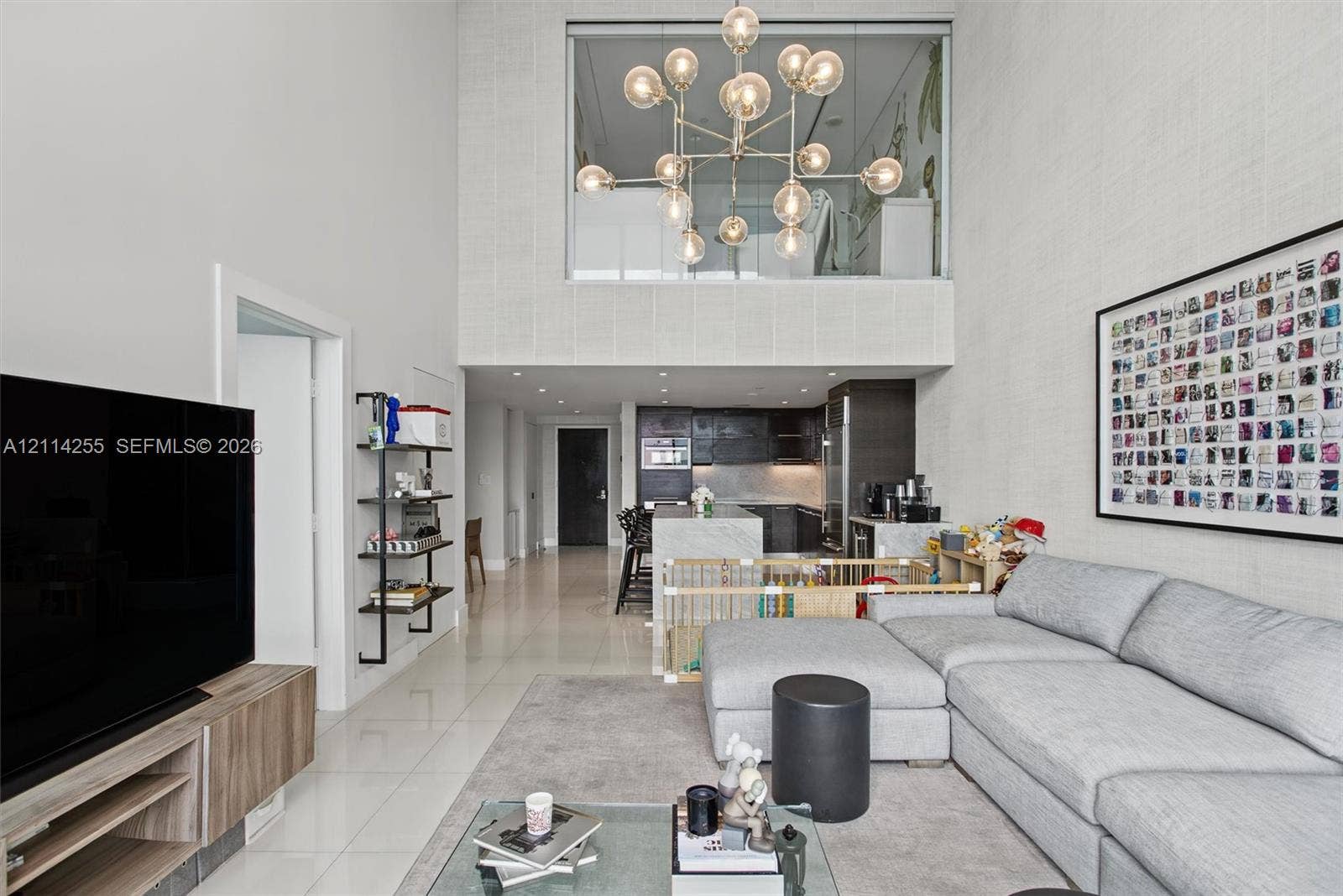900 Biscayne Boulevard, #1705, Miami, FL 33132 Double-height ceiling, large multi-globe chandelier, polished tile flooring, kitchen island with stone-finish waterfall edge, and textured wall finish