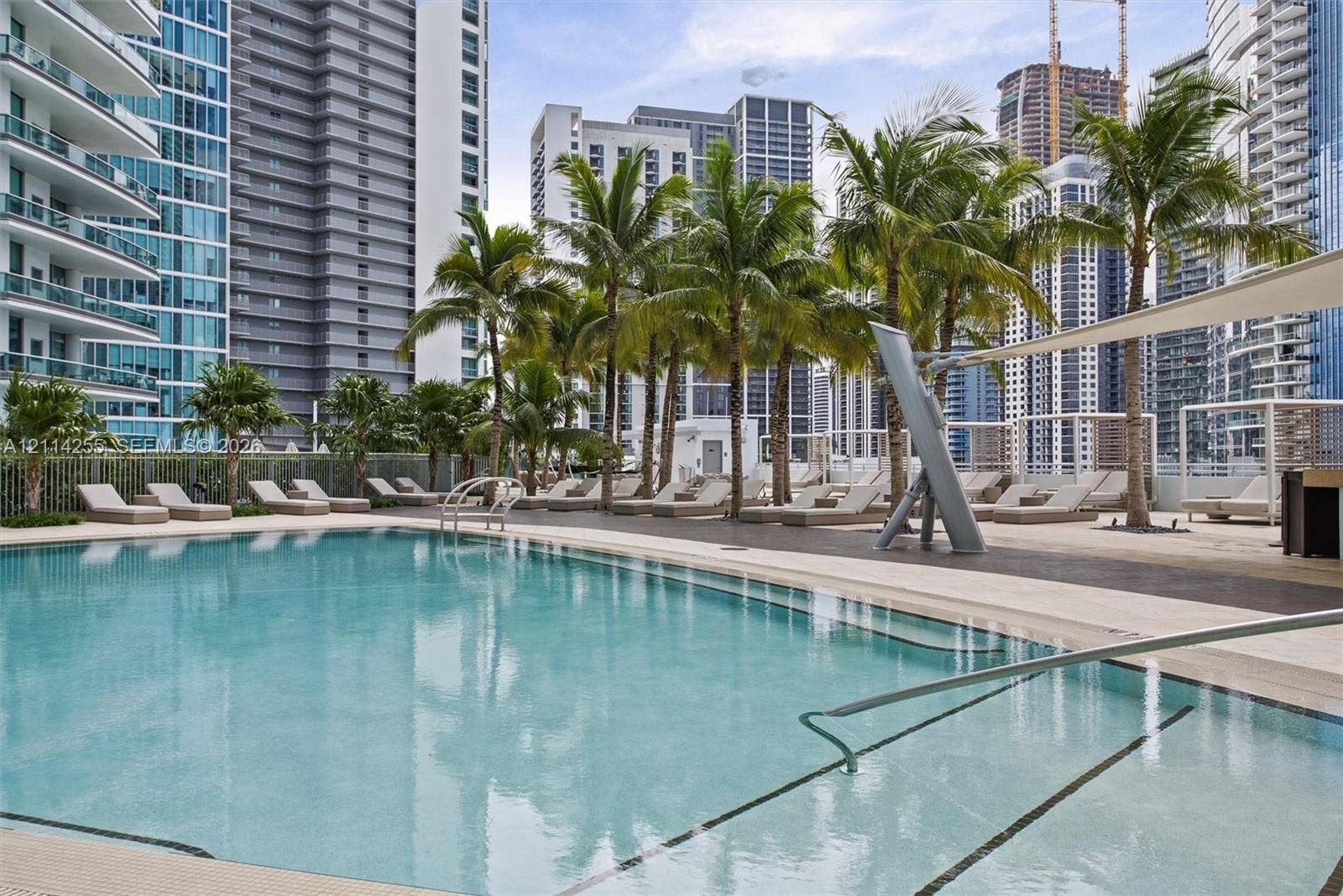 900 Biscayne Boulevard, #1705, Miami, FL 33132 Swimming pool featuring a sun deck, palm trees, and perimeter fencing, set against a backdrop of urban high-rise buildings