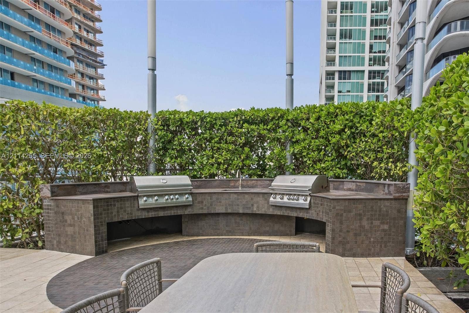 900 Biscayne Boulevard, #1705, Miami, FL 33132 Curved outdoor kitchen featuring dual stainless steel grills, a stone-tiled backsplash, and built-in prep counters, framed by integrated perimeter hedges