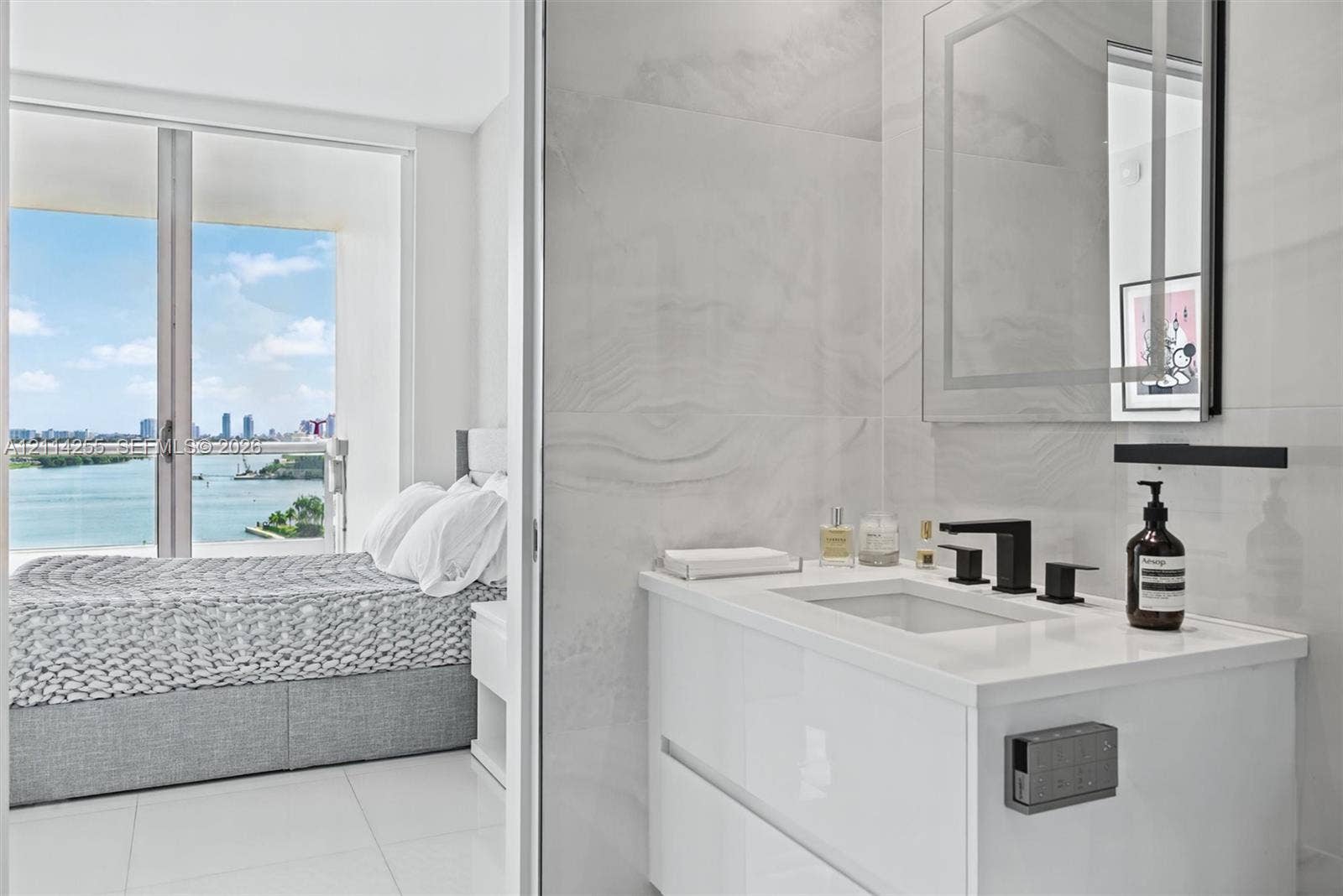 900 Biscayne Boulevard, #1705, Miami, FL 33132 Modern floating vanity with a solid-surface countertop, rectangular basin, and matte black faucet, featuring wall-to-wall large-format porcelain tile, a backlit mirror, and floor-to-ceiling glass sliding doors