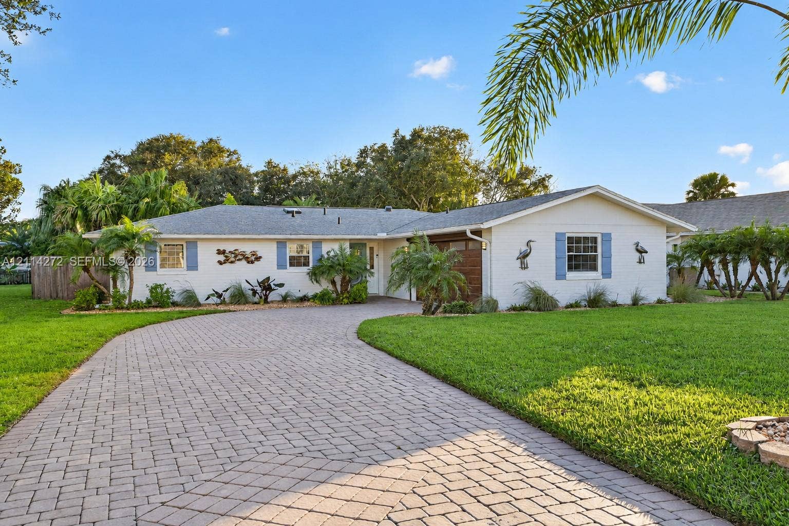 110 Cunningham, New Smyrna Beach, FL 32168 Single-story residence featuring a painted masonry exterior, a wide paver driveway, blue window shutters, and mature landscaping