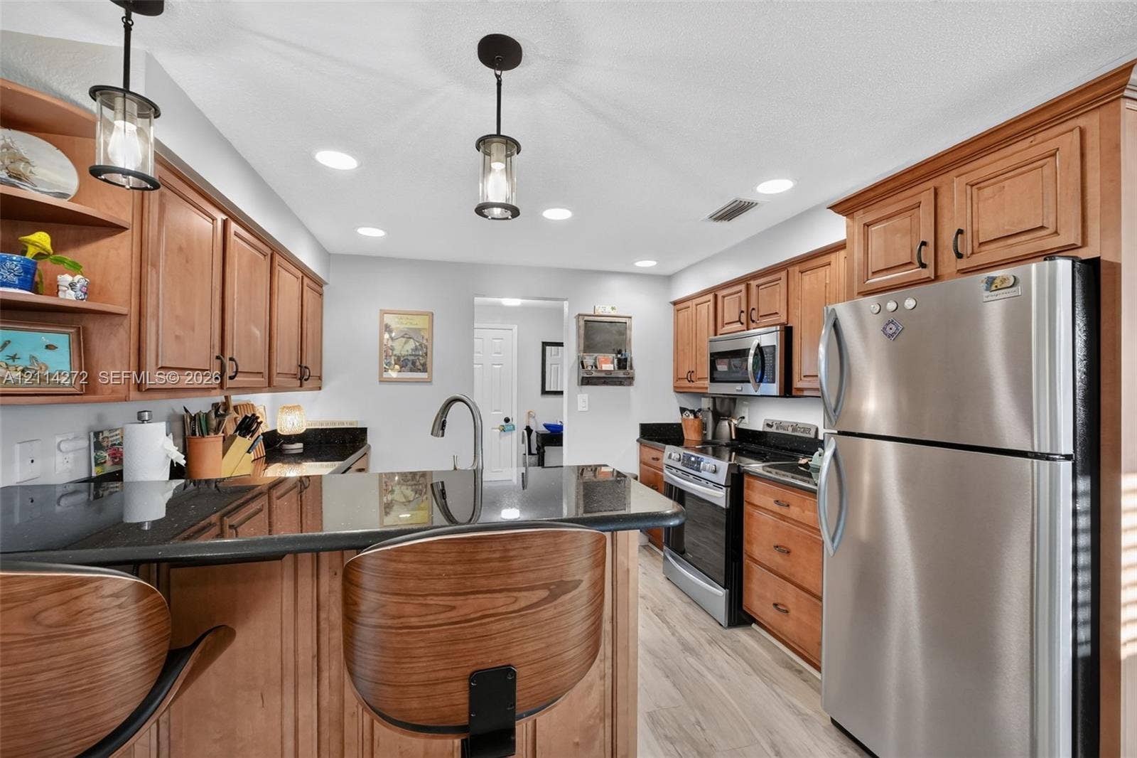 110 Cunningham, New Smyrna Beach, FL 32168 Kitchen featuring stained wood cabinetry, black countertops, stainless steel appliances, pendant lighting, and wood-finish flooring