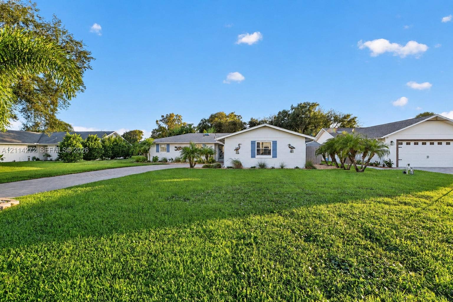 110 Cunningham, New Smyrna Beach, FL 32168 Single-story exterior featuring a light-toned facade, blue decorative window shutters, a paved driveway, and an attached multi-car garage