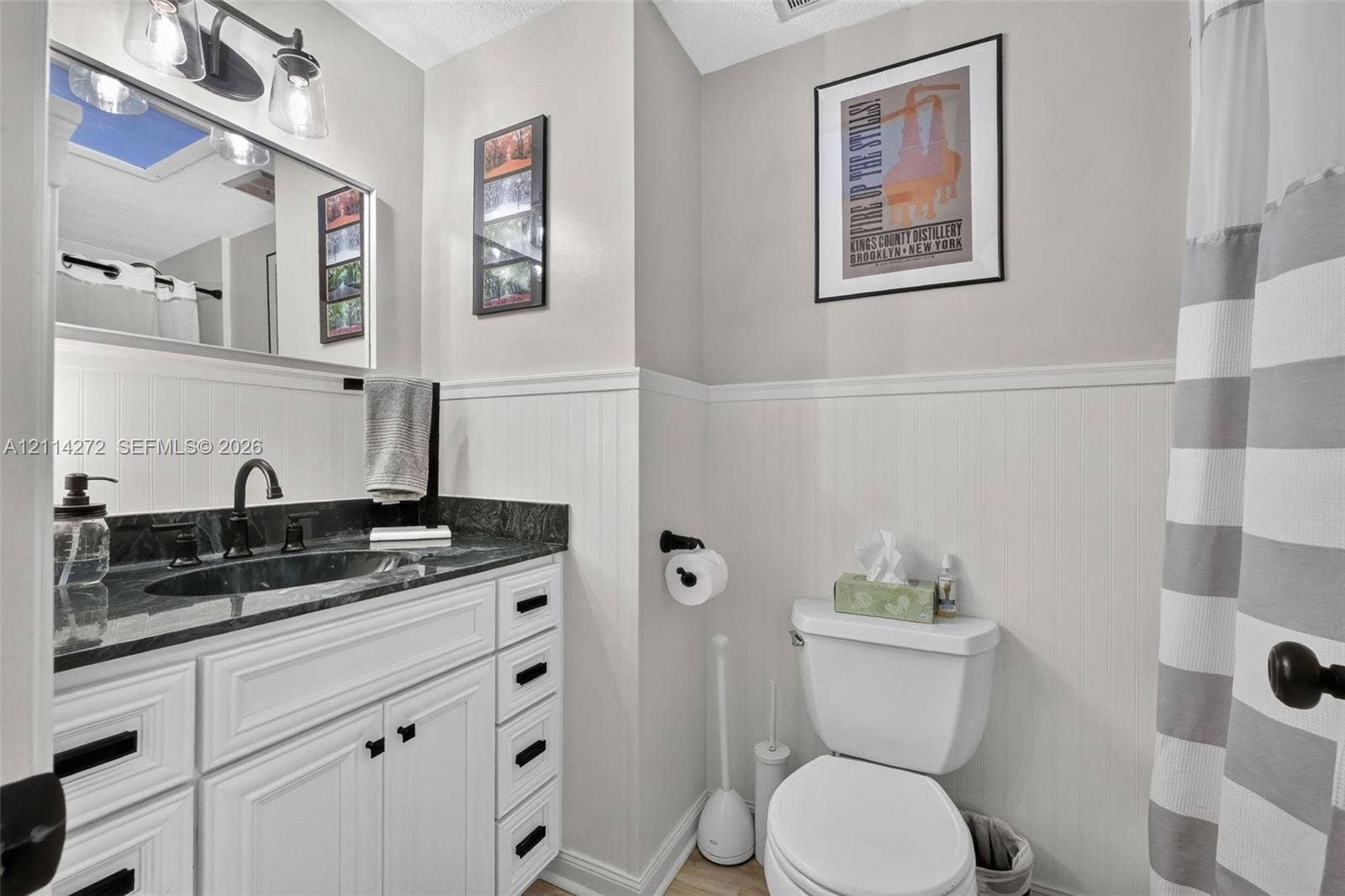 110 Cunningham, New Smyrna Beach, FL 32168 Bathroom featuring a vanity with dark stone countertop, integrated sink, white cabinetry with matte black hardware, and white beadboard wainscoting