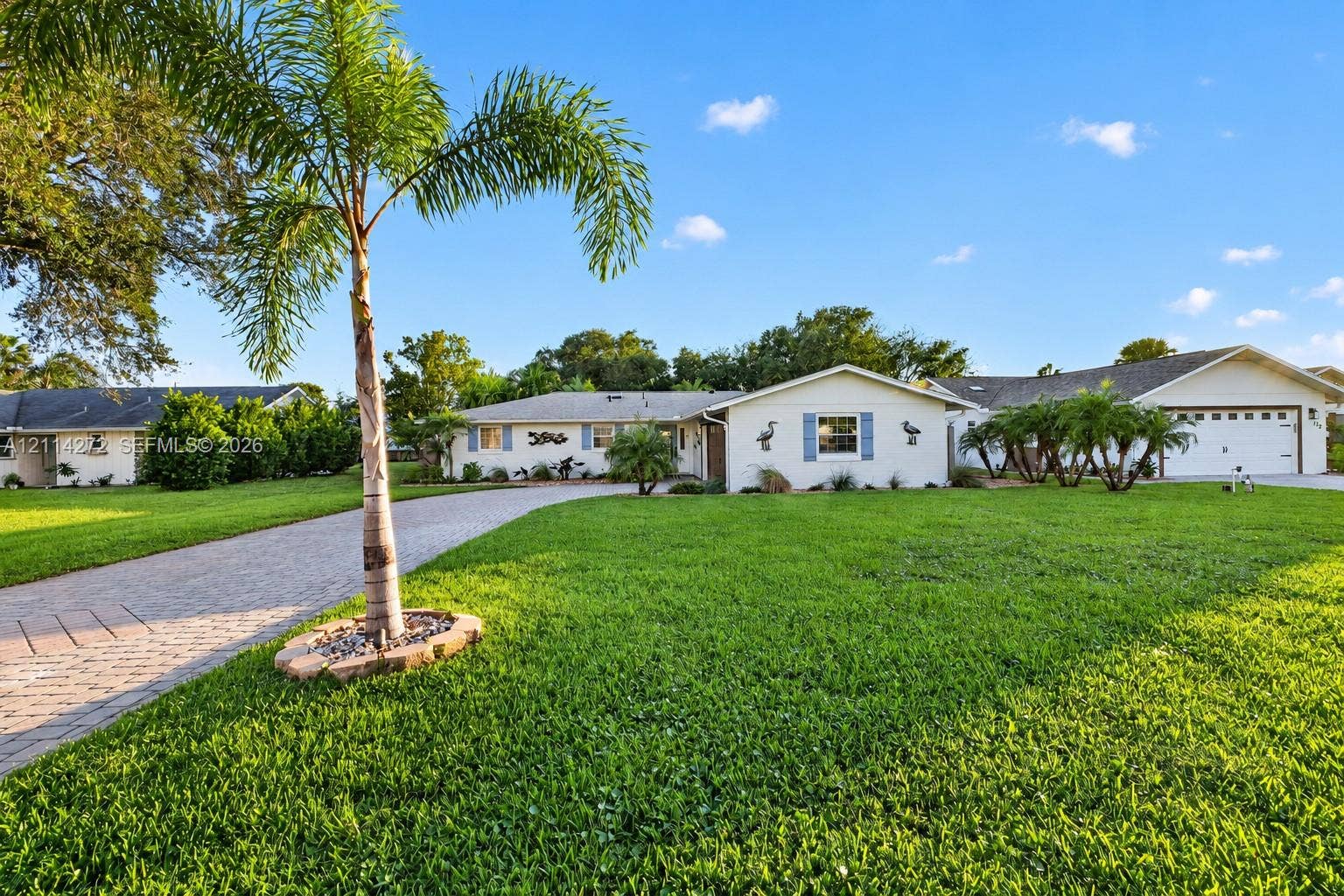 110 Cunningham, New Smyrna Beach, FL 32168 Single-story exterior featuring a paver driveway, manicured lawn, attached two-car garage, and mature palm landscaping