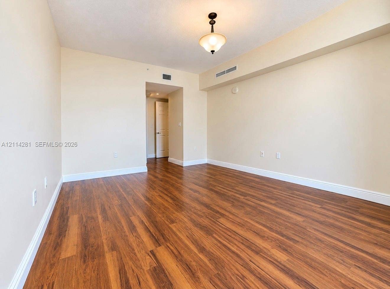 Neutral-toned interior space featuring wood-finish flooring, recessed ceiling lighting, and a suspended semi-flush mount fixture