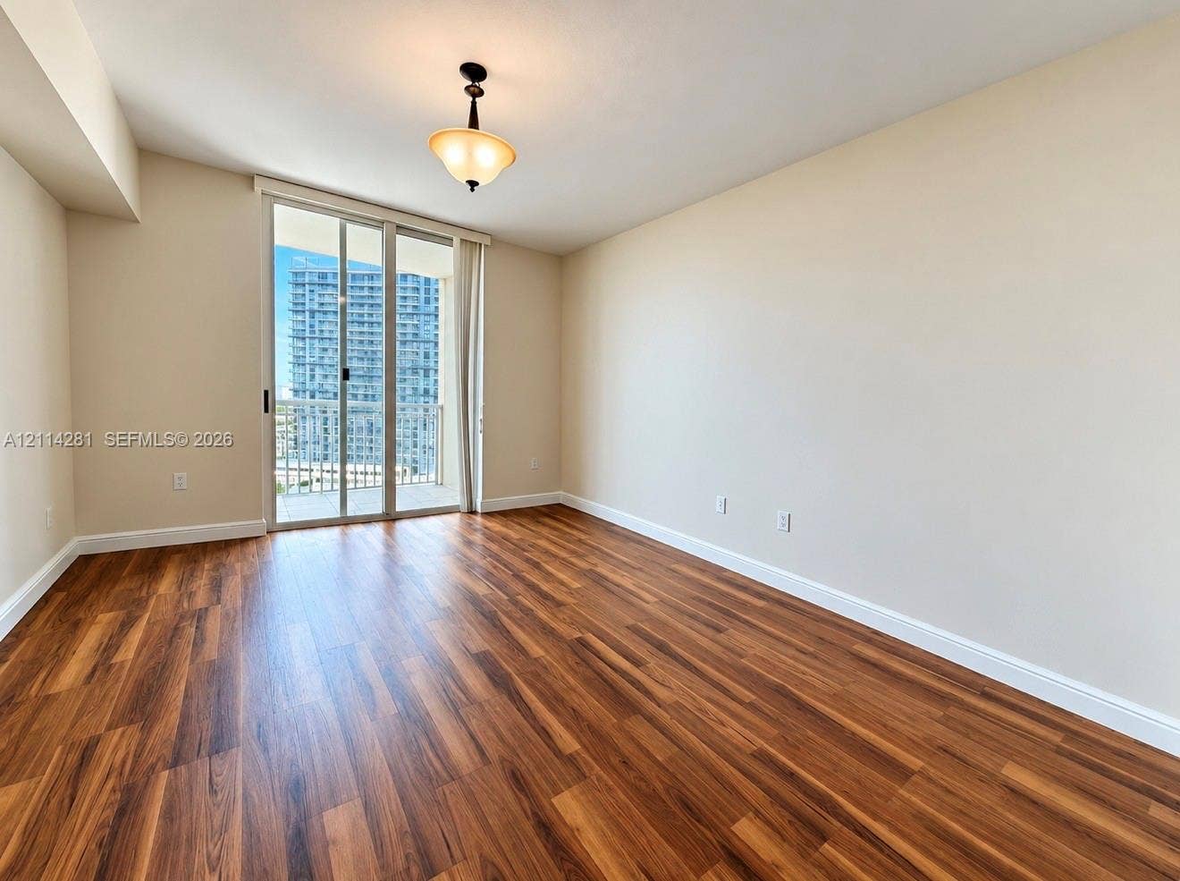 Interior room featuring wood-finish flooring, neutral wall paint, a semi-flush mount light fixture, and a sliding glass door providing access to an exterior balcony