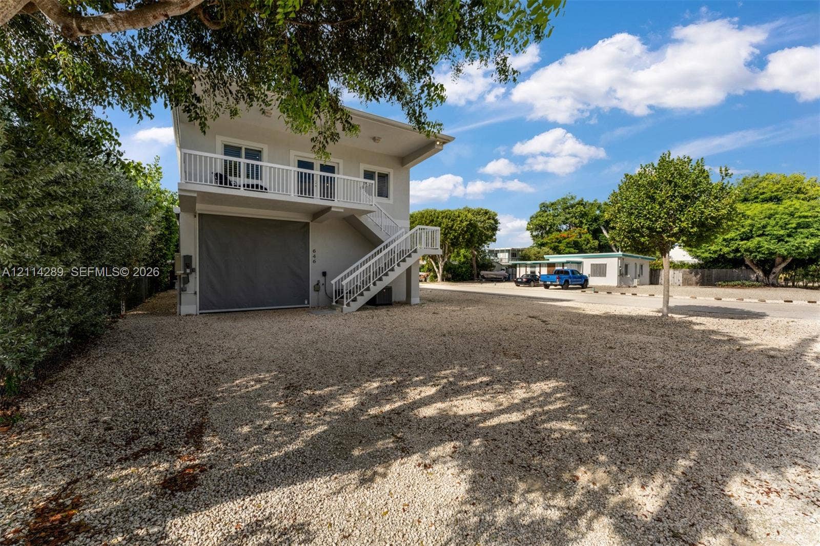 646 Cabrera Street, Key Largo, FL 33037 Two-story exterior featuring a gravel driveway, an integrated ground-level garage, and an elevated balcony with white railings and exterior staircase