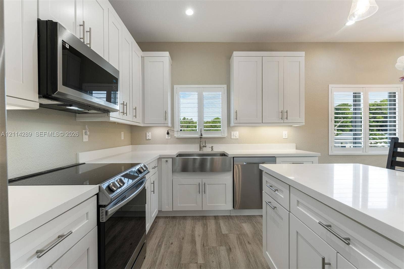 646 Cabrera Street, Key Largo, FL 33037 Kitchen featuring white shaker-style cabinetry, quartz countertops, a stainless steel apron-front sink, stainless steel appliances, and wood-finish flooring