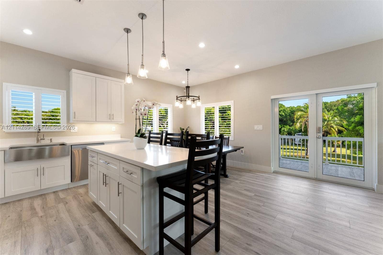 646 Cabrera Street, Key Largo, FL 33037 Kitchen featuring white cabinetry, an expansive center island with stone countertop, stainless steel farmhouse sink, wood-finish flooring, and glass-paned double doors with exterior deck access