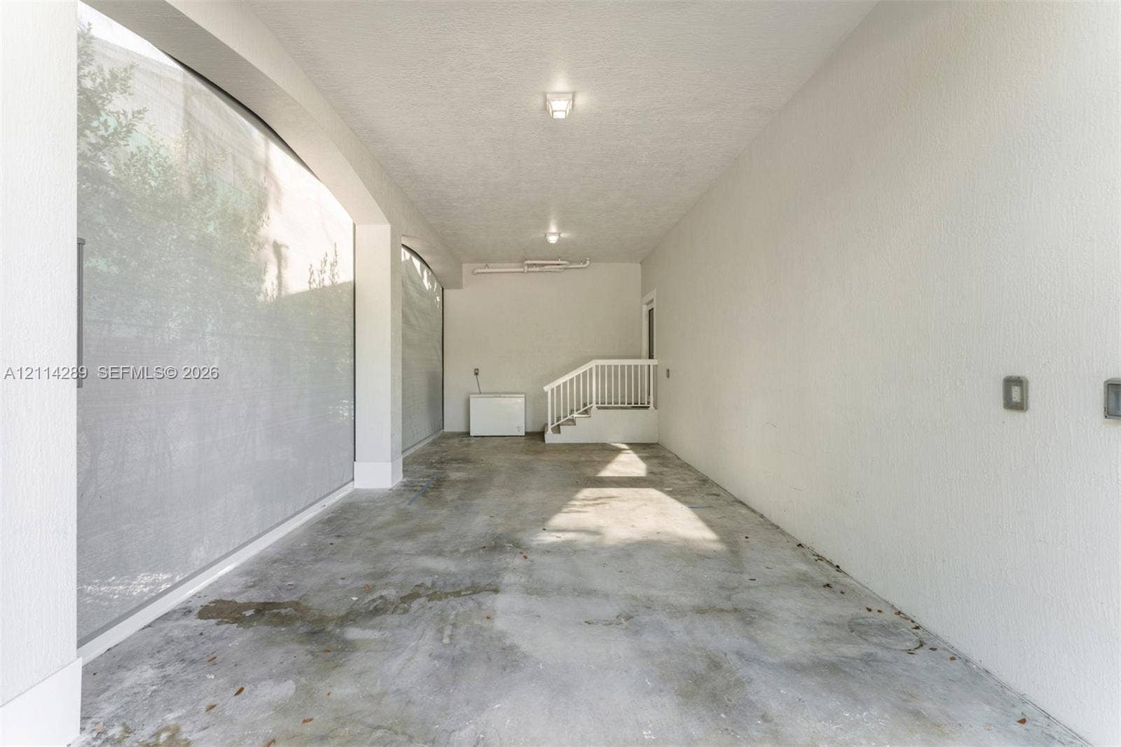 646 Cabrera Street, Key Largo, FL 33037 Covered parking area featuring textured concrete flooring, white stucco walls, overhead lighting, and built-in white railings
