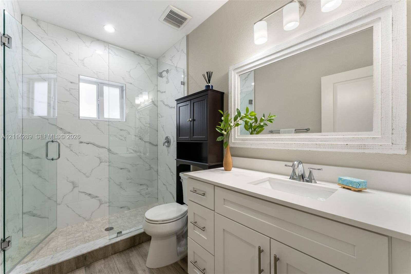 646 Cabrera Street, Key Largo, FL 33037 Bathroom featuring a white vanity with a rectangular undermount sink, stone-finish countertop, walk-in shower with floor-to-ceiling tile surround, glass enclosure, and wood-finish flooring