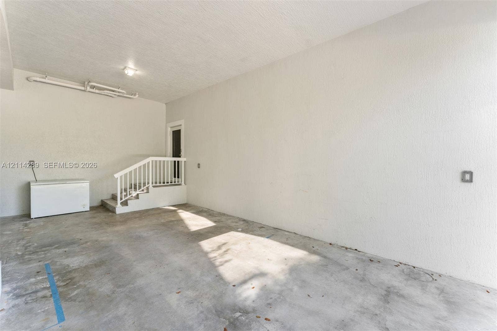 646 Cabrera Street, Key Largo, FL 33037 Enclosed garage space featuring a concrete floor, textured walls, and a staircase with a white railing