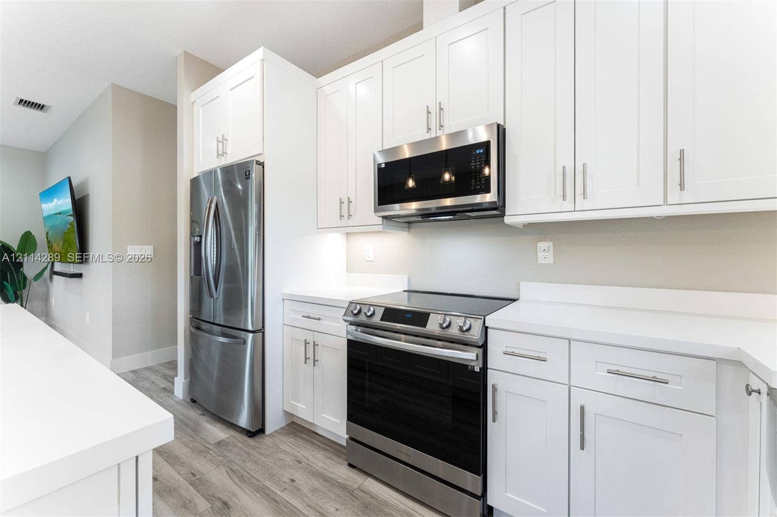 646 Cabrera Street, Key Largo, FL 33037 Kitchen featuring white cabinetry, solid-surface countertops, wood-finish flooring, and a stainless steel appliance suite including a built-in microwave and range