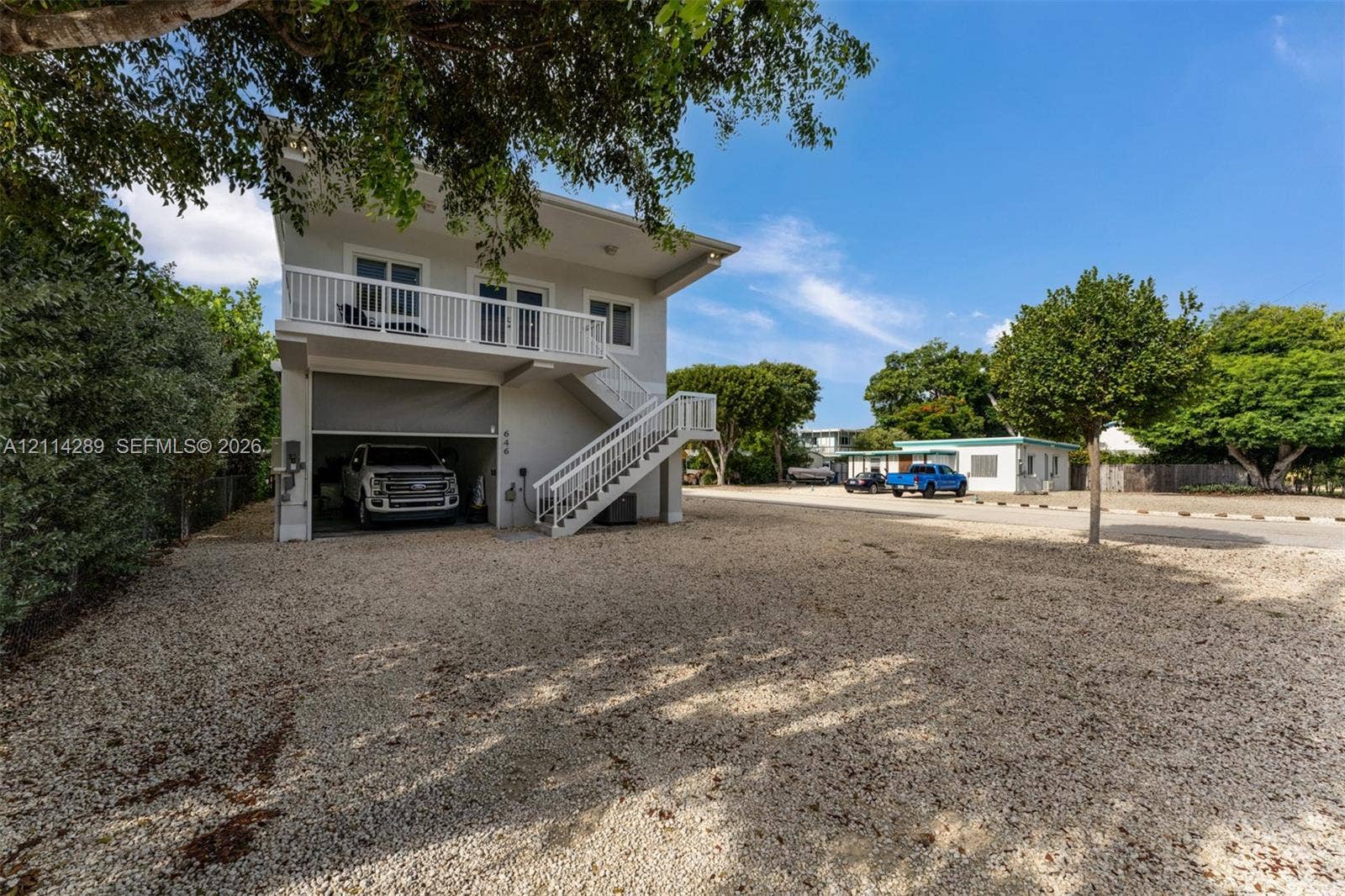 646 Cabrera Street, Key Largo, FL 33037 Two-story exterior featuring a gravel driveway, an open-concept ground-level garage, and a second-story balcony with white railing and external staircase access