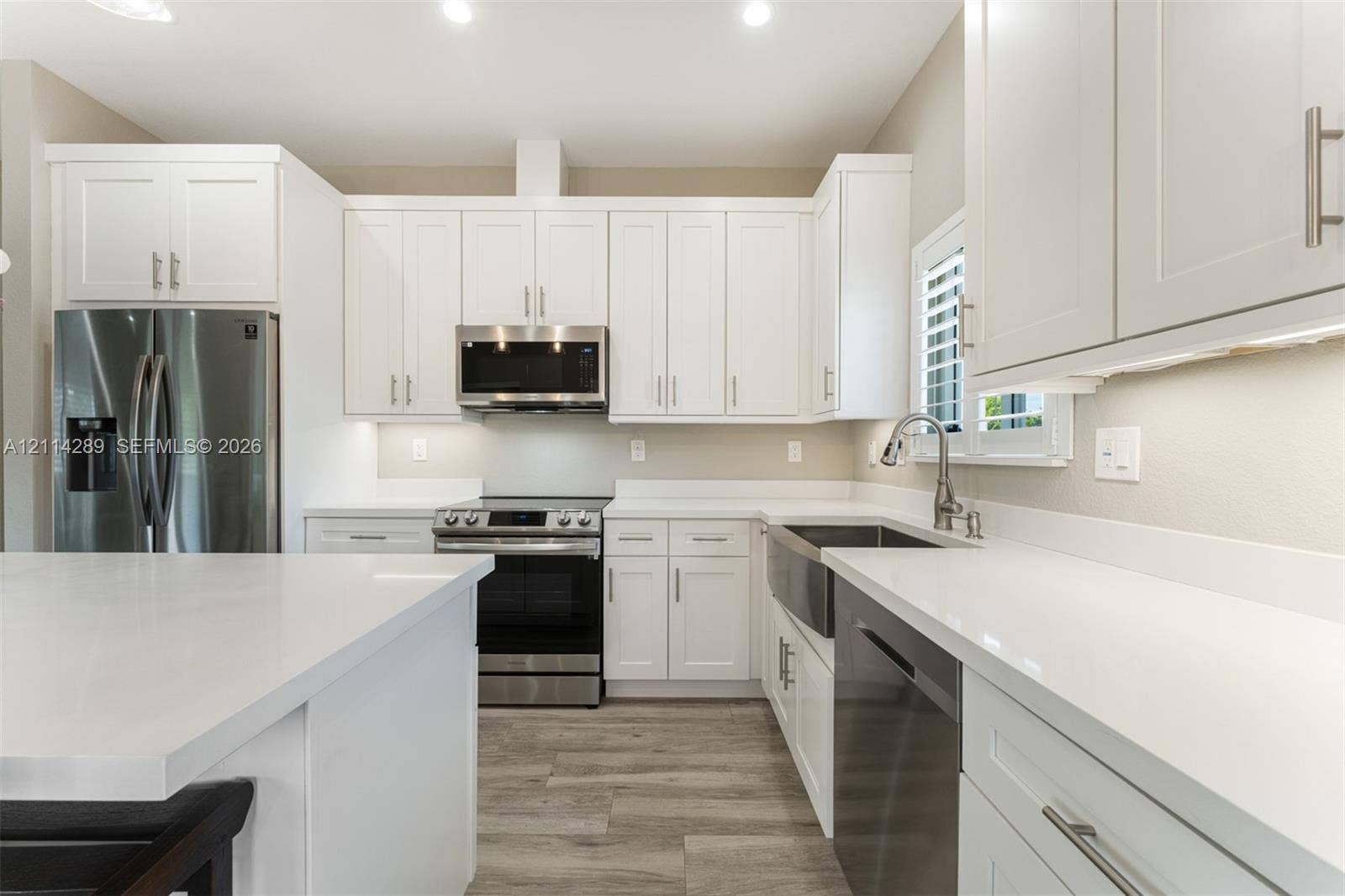 646 Cabrera Street, Key Largo, FL 33037 Kitchen featuring white shaker-style cabinetry, quartz countertops, a farmhouse-style stainless steel sink, stainless steel appliances, and wood-finish flooring