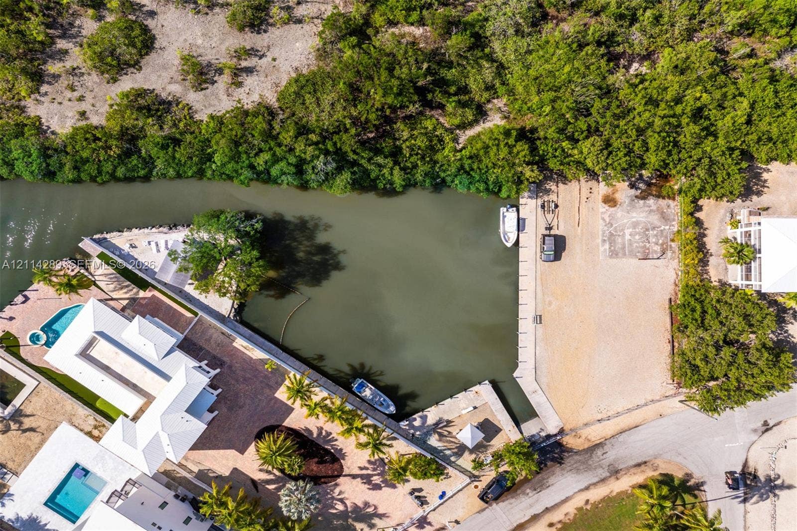 646 Cabrera Street, Key Largo, FL 33037 Aerial perspective of a waterfront property featuring a deep-water boat slip, a private canal bulkhead, an in-ground swimming pool, and paved patio surfaces