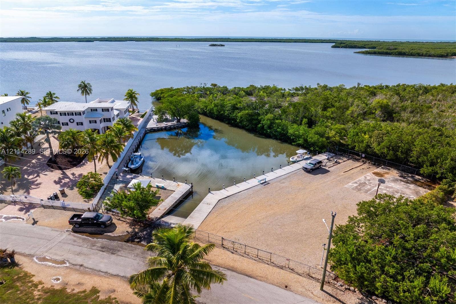 646 Cabrera Street, Key Largo, FL 33037 Waterfront property featuring a private concrete boat slip, gravel lot, perimeter fencing, and mature palm trees