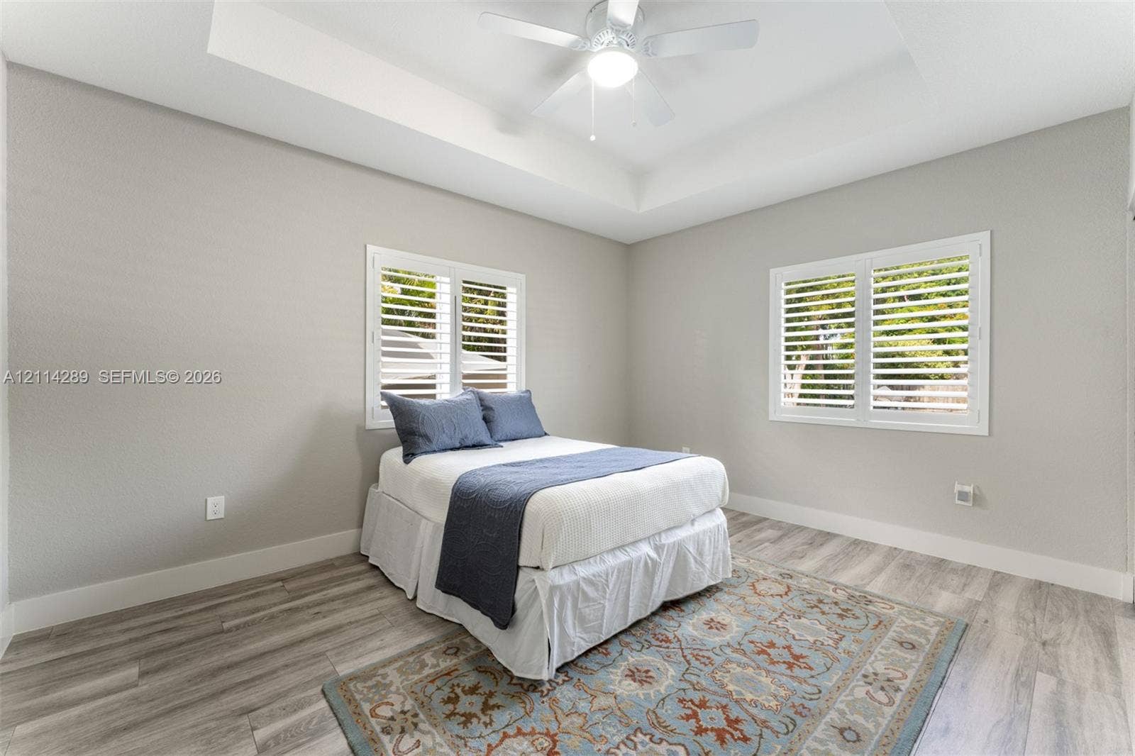 646 Cabrera Street, Key Largo, FL 33037 Tray ceiling with a central white ceiling fan, wood-finish flooring, and white plantation shutters on dual windows