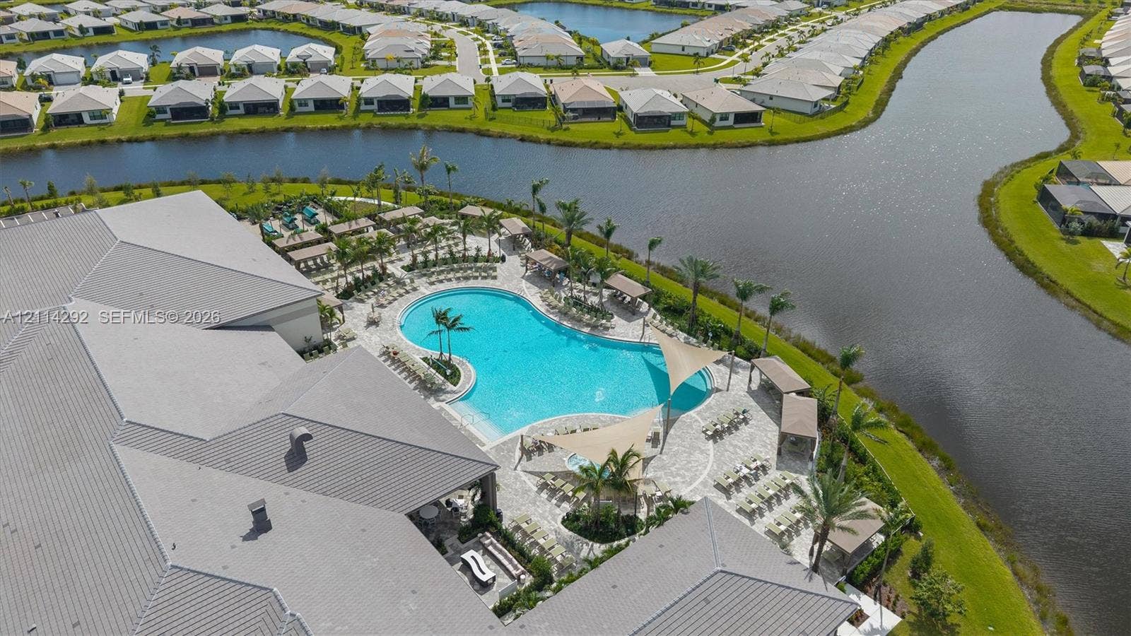 Aerial perspective of a community facility featuring a resort-style swimming pool, paver-stone pool deck, shade structures, and waterfront positioning
