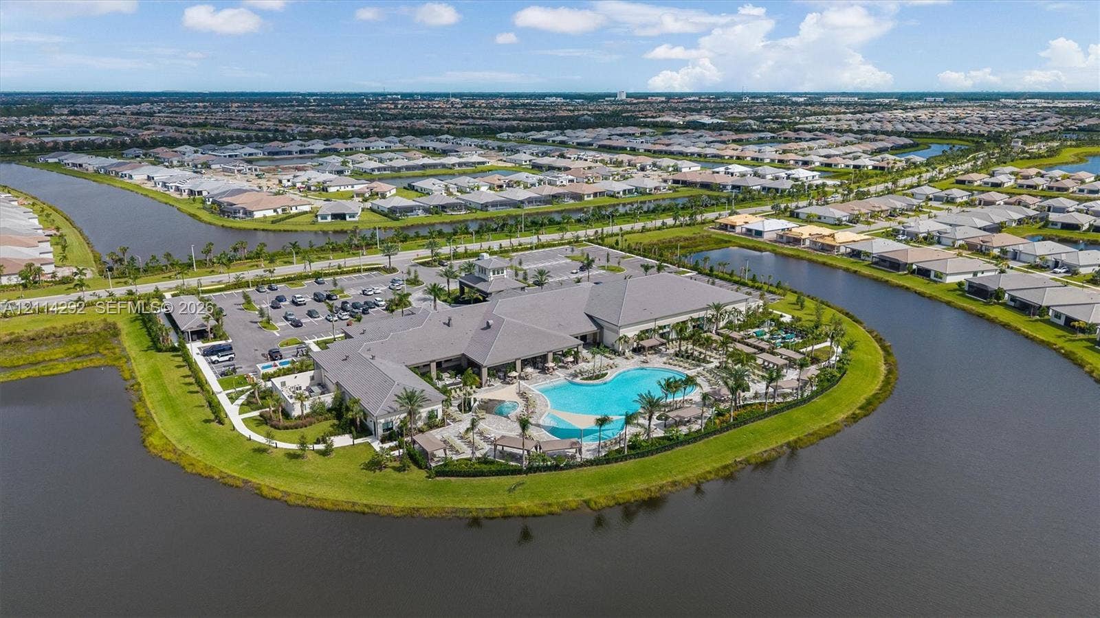 Community clubhouse featuring an expansive swimming pool, paved sundeck, surrounding water features, and manicured landscaping