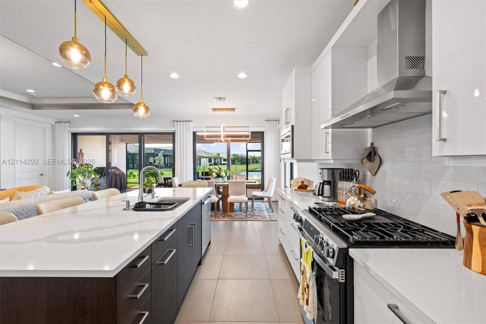 Kitchen featuring a central island with quartz countertops, high-gloss cabinetry, a stainless steel range hood, and pendant lighting