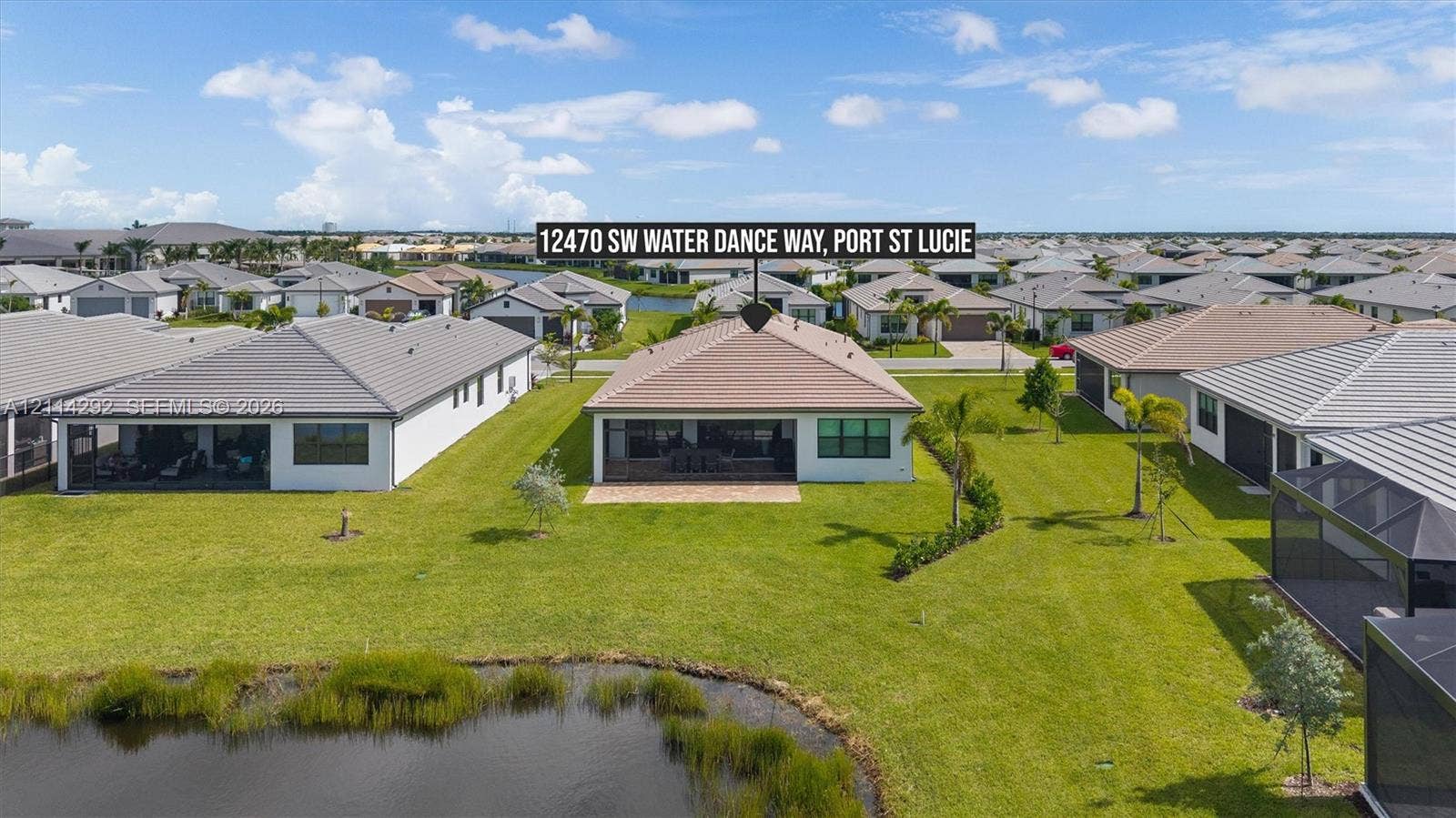 Aerial perspective of a residential property featuring a tiled roof, screened rear patio, and expansive lawn area backing to a waterfront pond