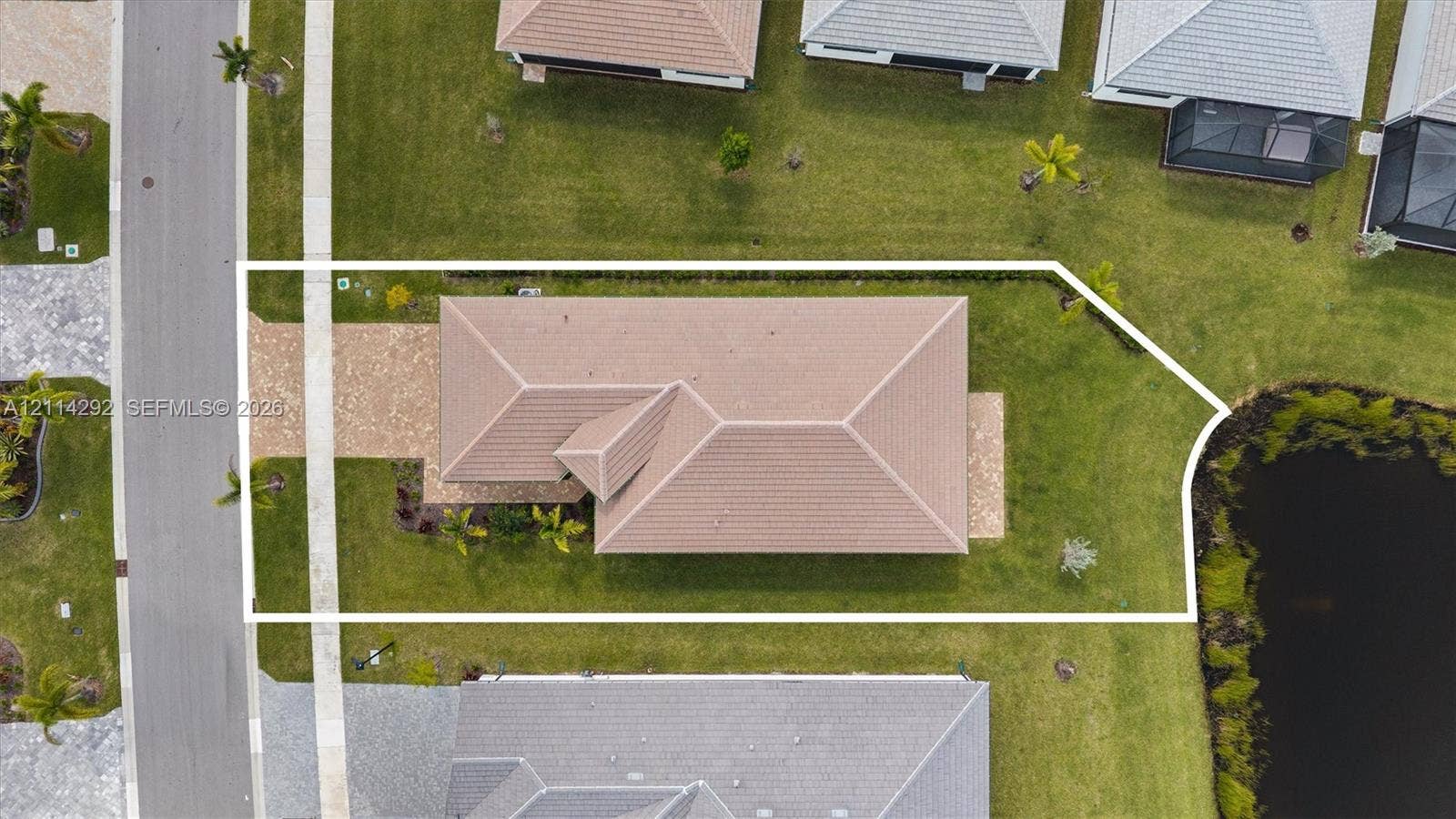 Aerial perspective of a property featuring a concrete tile roof, paver driveway, grass lawn, and waterfront positioning