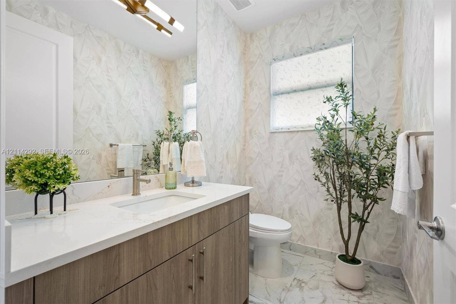Bathroom featuring a wood-finish vanity with a stone-surface countertop, rectangular undermount sink, patterned wall covering, and polished stone-finish floor tile