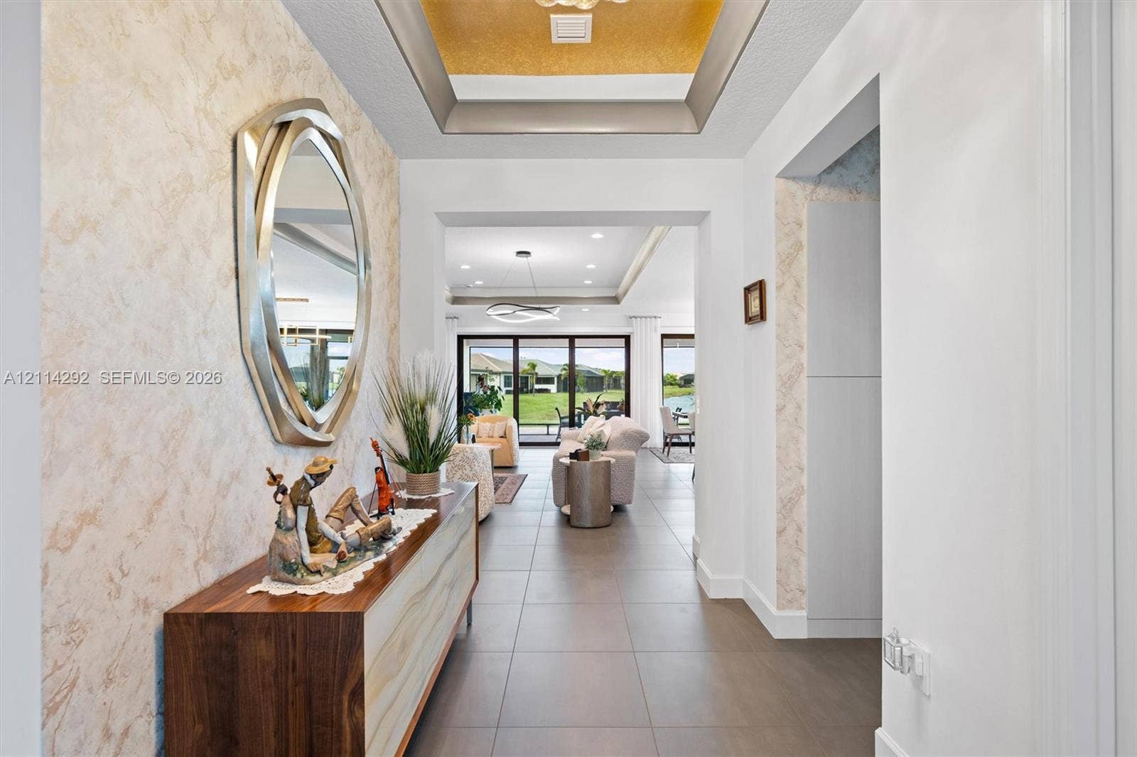 Foyer featuring a recessed tray ceiling with metallic finish, textured wall detailing, and large-format tile flooring