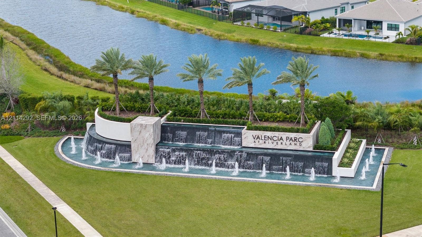 Community entrance feature incorporating multi-tiered stone-finish wall, cascading water fountain, palm tree landscaping, and surrounding canal