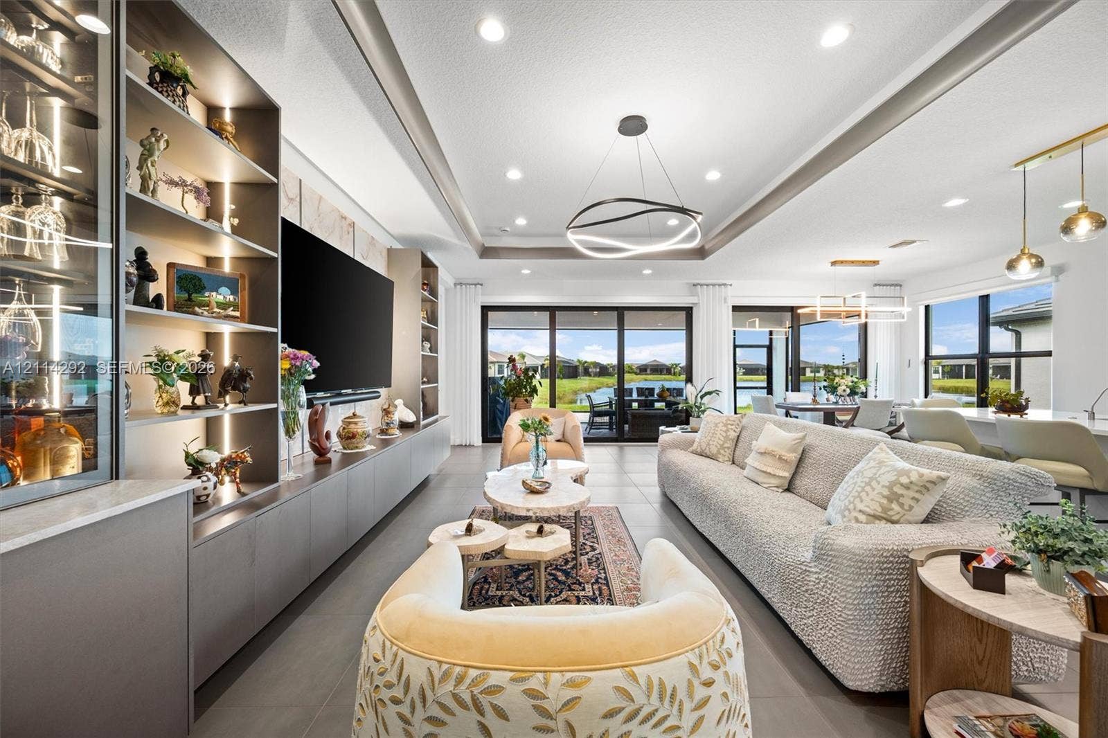 Open-concept living space featuring a floor-to-ceiling built-in cabinetry unit with integrated lighting, a recessed tray ceiling with modern LED fixtures, and large multi-panel sliding glass doors