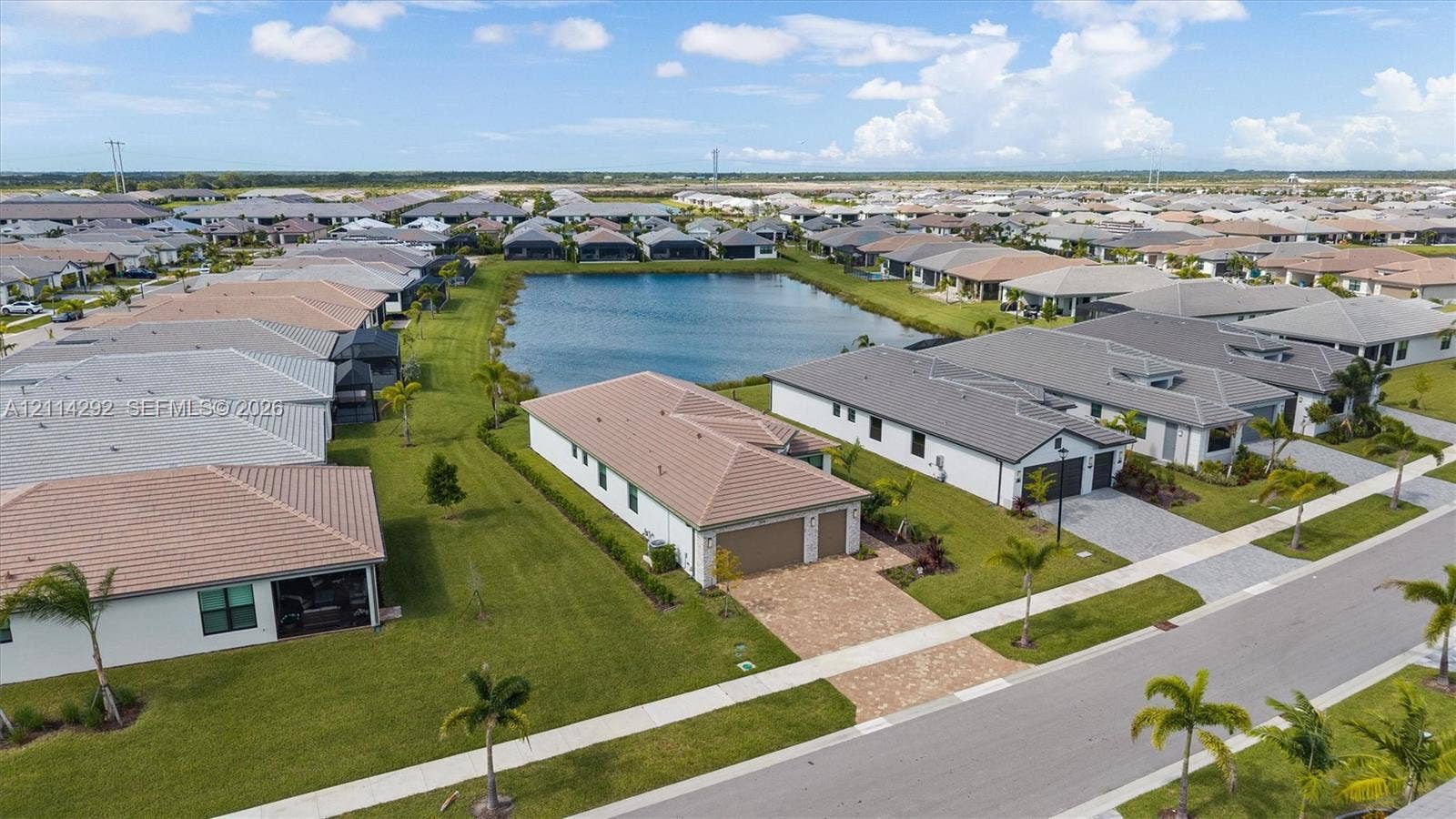 Aerial perspective featuring a waterfront property with a tiled roof, paved driveway, two-car garage, and established landscaping