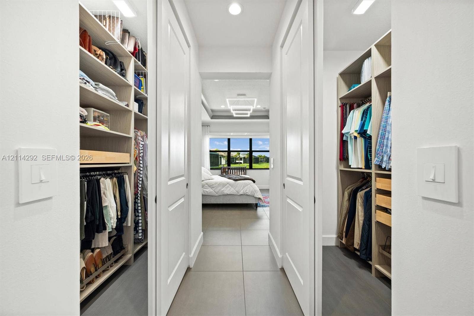 Walk-in closet featuring floor-to-ceiling built-in shelving, hanging rods, pull-out storage drawers, and large-format tile flooring