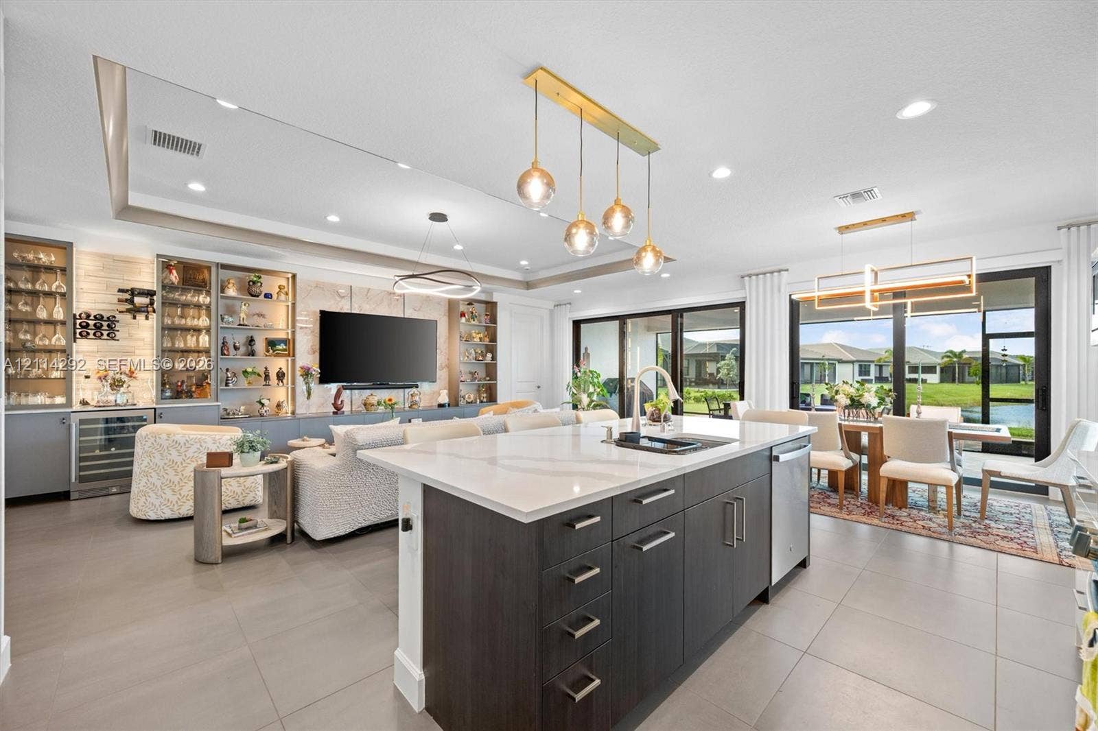 Center island with quartz countertop and undermount sink, dark-toned cabinetry, built-in display shelving with integrated lighting, oversized sliding glass doors, and recessed ceiling lighting