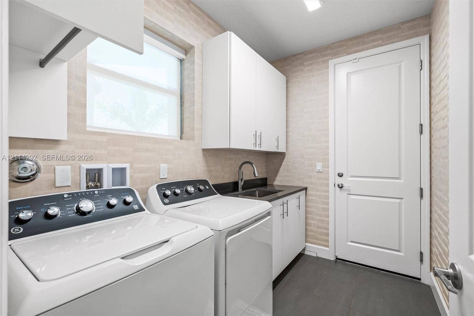 Utility room featuring textured wall tile, white shaker-style cabinetry, a dark countertop with a built-in sink, and slate-finish flooring