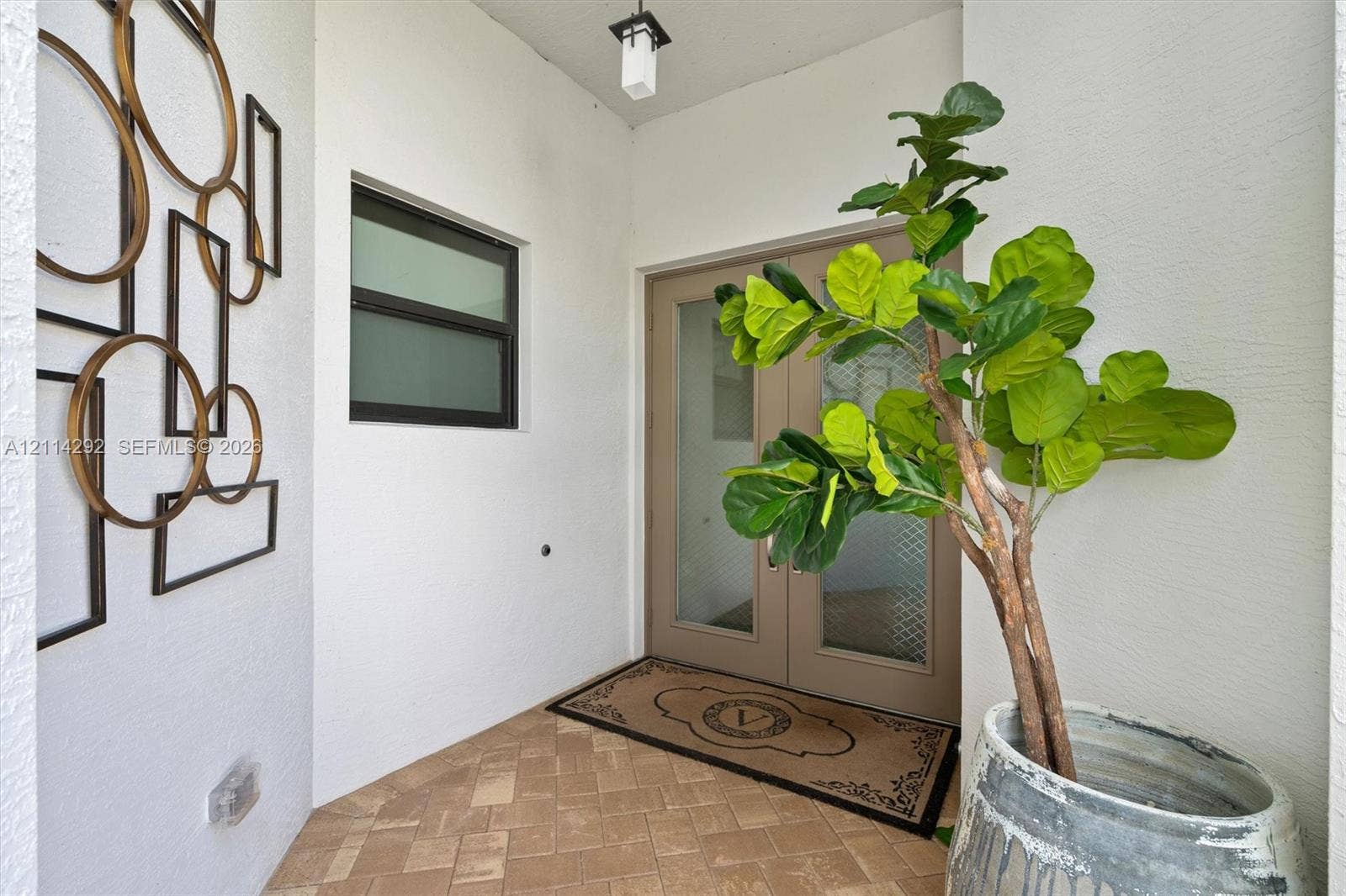 Covered entryway featuring herringbone-patterned stone flooring, a double-door entry with frosted glass inserts, and a contemporary ceiling-mounted lantern fixture