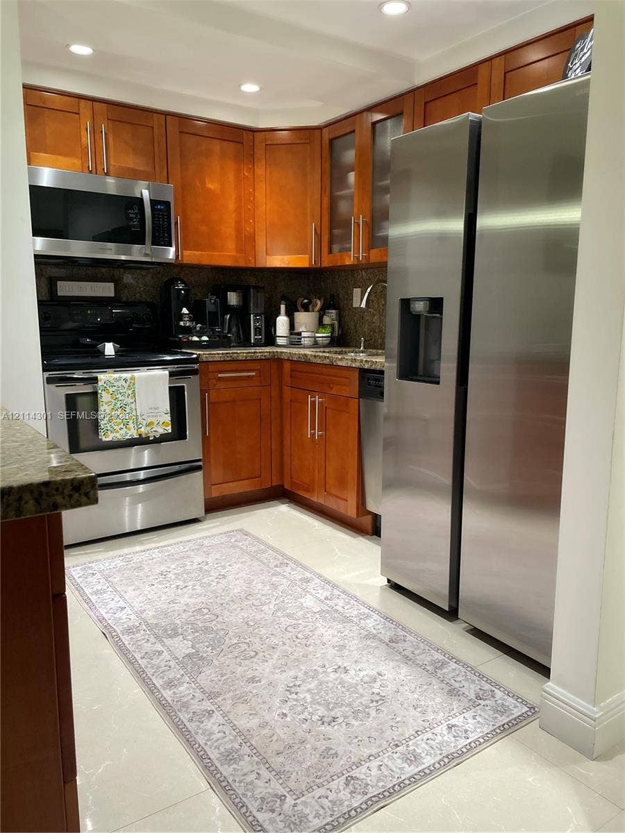 Kitchen featuring wood-finish cabinetry, stone-surface countertops, stainless steel appliances, glass-front upper cabinet doors, and recessed lighting