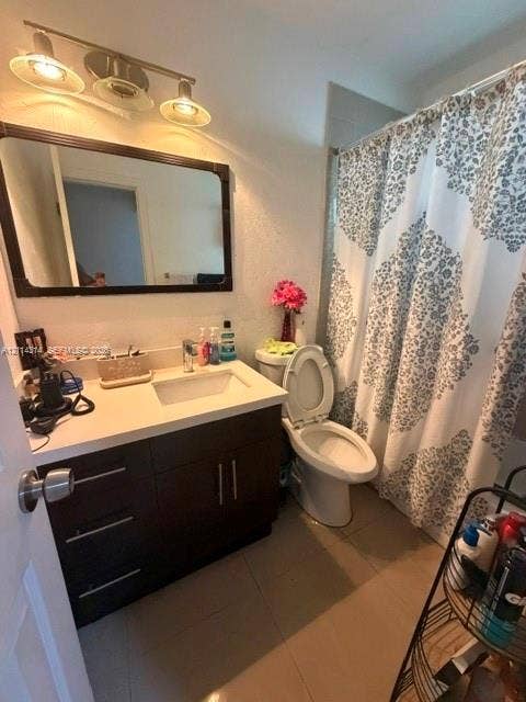 2312 Van Buren Street, #11, Hollywood, FL 33020 Bathroom featuring a vanity with a white countertop and rectangular undermount sink, dark-toned cabinetry with modern hardware, a rectangular wall-mounted mirror, three-light vanity fixture, and tiled flooring
