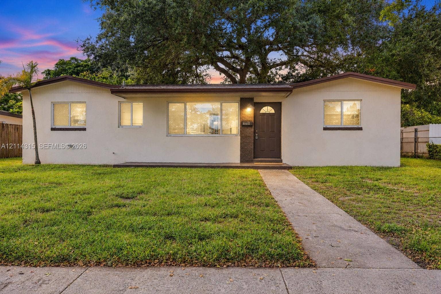 340 N 68th Avenue, Hollywood, FL 33024 Single story exterior featuring a light-toned stucco facade, dark-finish entry door, low-pitch roofline, expansive front lawn, and mature canopy trees