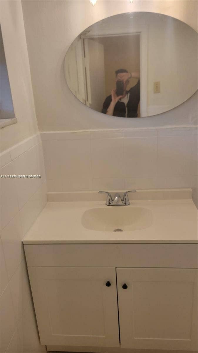 2131 N 19th Avenue, #2133, Hollywood, Hollywood, FL 33020 Bathroom vanity featuring a solid-surface countertop, an integrated sink basin, chrome dual-handle faucet, oval mirror, and tiled wall surround