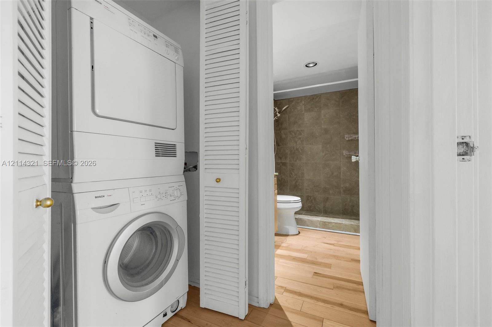 10350 W Bay Harbor Drive, #9C, Bay Harbor Islands, FL 33154 Stacked washer and dryer unit concealed behind white louvered doors, featuring wood-finish flooring and recessed ceiling lighting