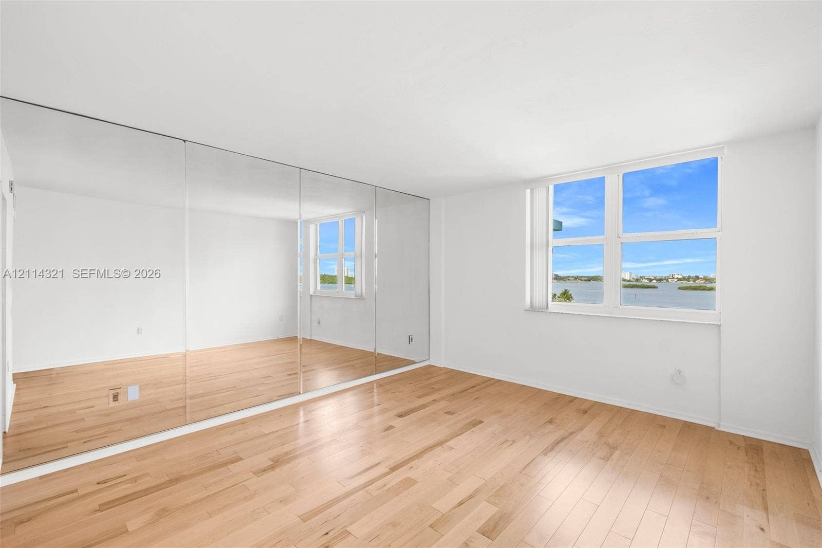 10350 W Bay Harbor Drive, #9C, Bay Harbor Islands, FL 33154 Bright room featuring wood-finish flooring, a floor-to-ceiling mirrored wall, and large windows with water scenery