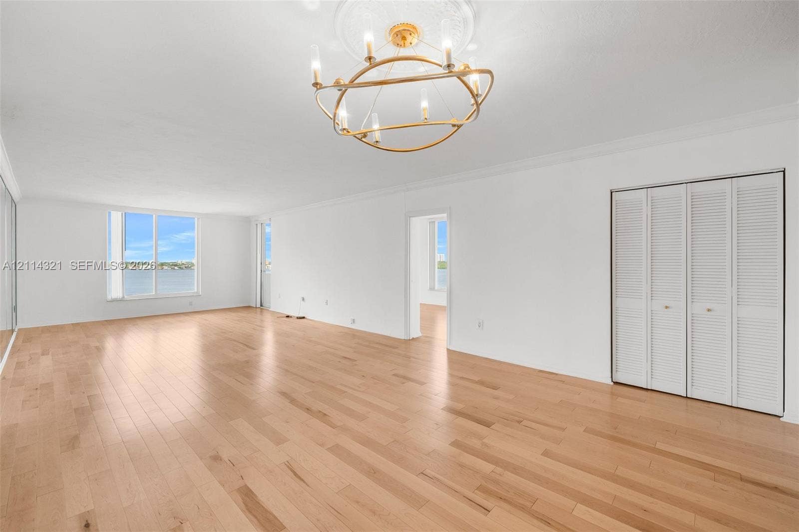 10350 W Bay Harbor Drive, #9C, Bay Harbor Islands, FL 33154 Open-concept interior featuring wood-finish flooring, gold-tone chandelier with decorative ceiling medallion, floor-to-ceiling windows, and bifold closet doors