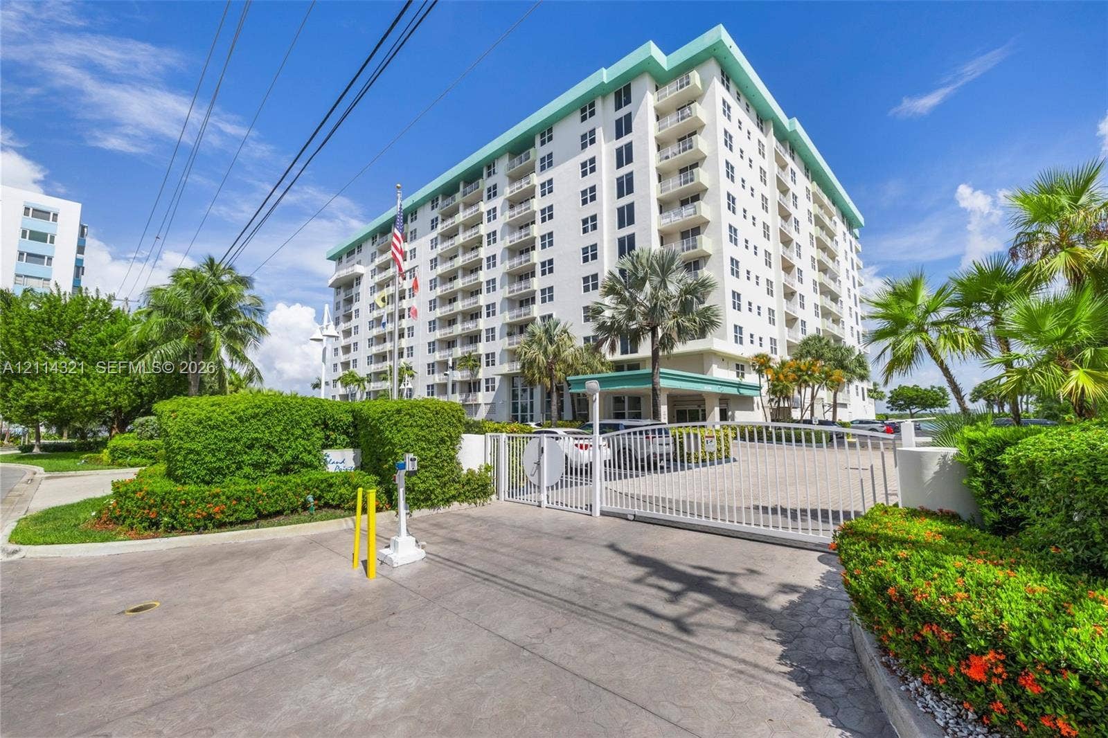 10350 W Bay Harbor Drive, #9C, Bay Harbor Islands, FL 33154 High-rise residential exterior featuring a gated entry, concrete-paved driveway, multi-level balconies, and mature tropical landscaping