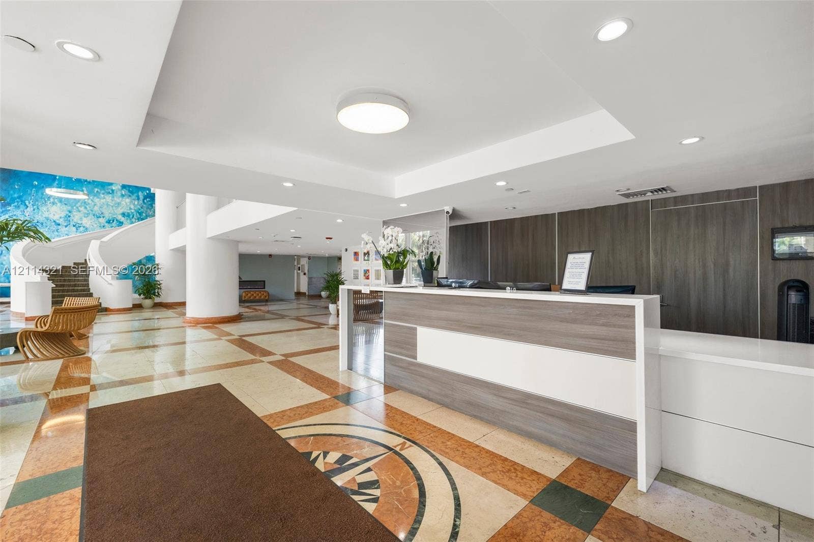 10350 W Bay Harbor Drive, #9C, Bay Harbor Islands, FL 33154 Lobby area featuring a custom reception desk with composite surfacing, recessed lighting, multi-toned stone flooring with inlaid compass motif, and a spiral staircase