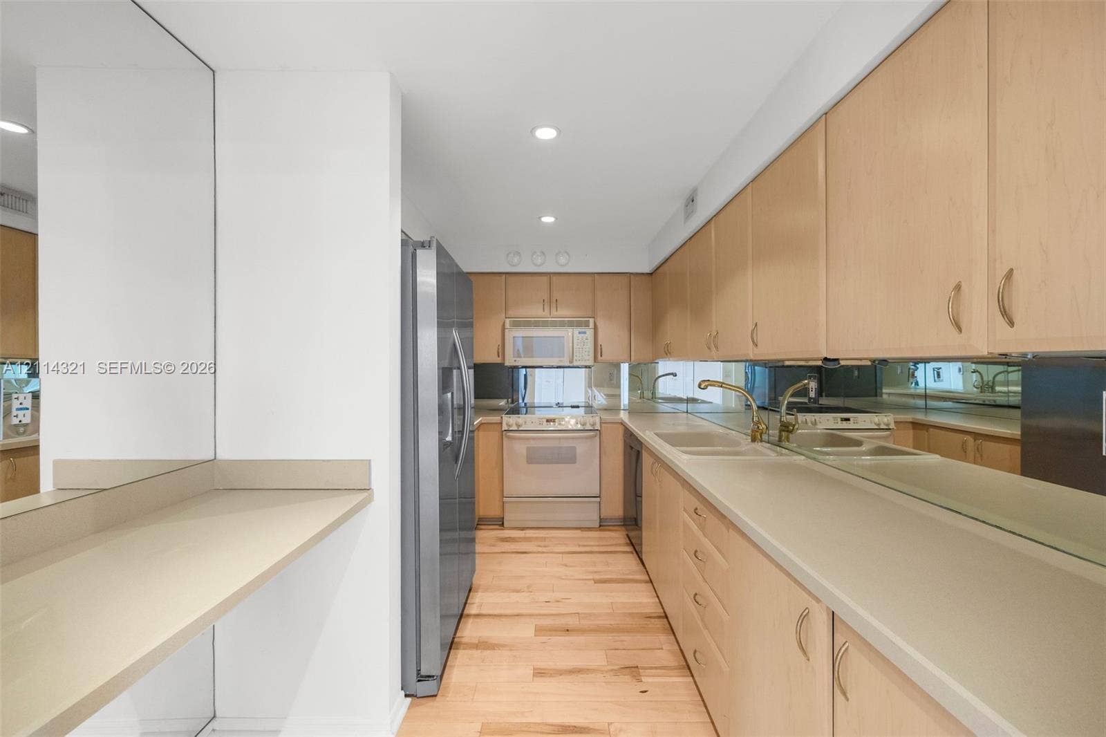 10350 W Bay Harbor Drive, #9C, Bay Harbor Islands, FL 33154 Kitchen featuring flat-panel wood cabinetry, solid-surface countertops, wood-finish flooring, full-height mirror backsplash, and stainless steel refrigerator