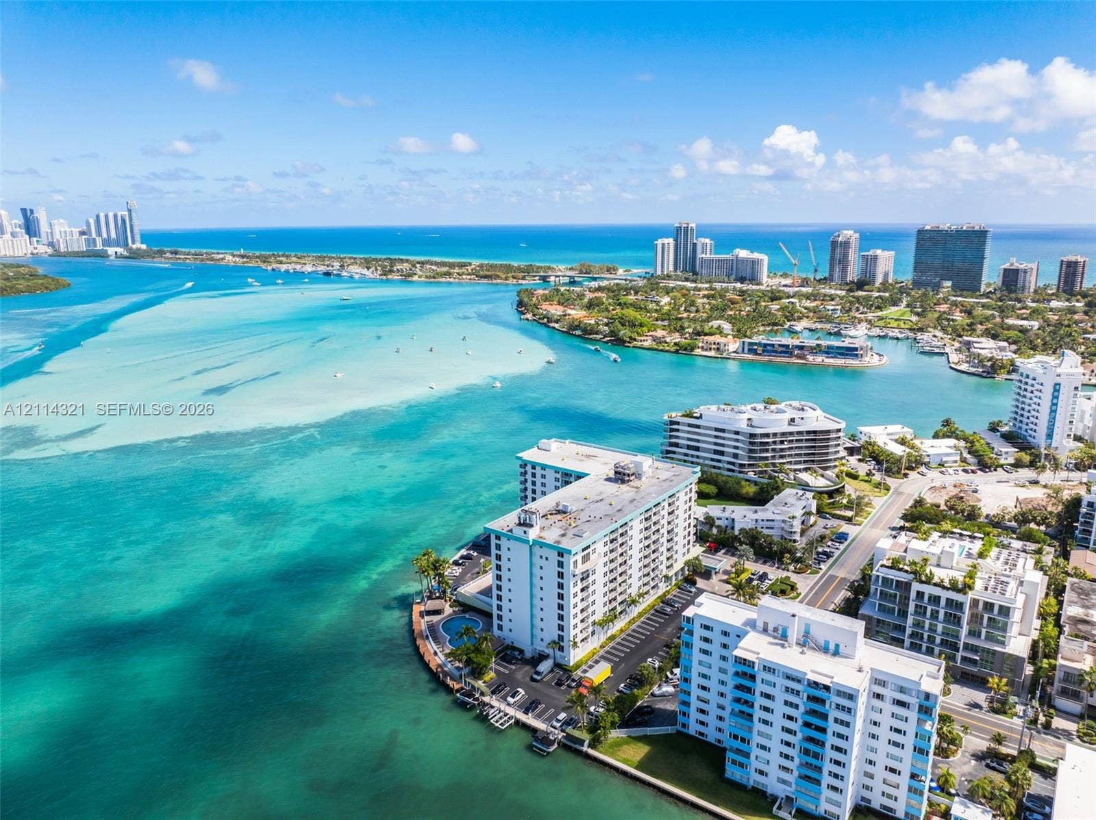 10350 W Bay Harbor Drive, #9C, Bay Harbor Islands, FL 33154 Aerial perspective of a multi-story residential building situated on a waterfront peninsula featuring a swimming pool, paved surface parking, and coastal water surroundings